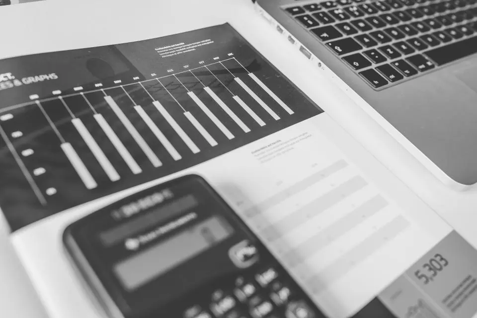 Calculator, bar charts and a laptop on a desk, in black and white
