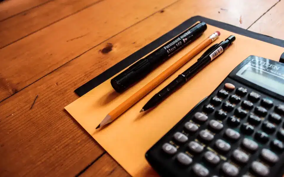 Calculator, pencils and a marker on a document folder on a wooden desk